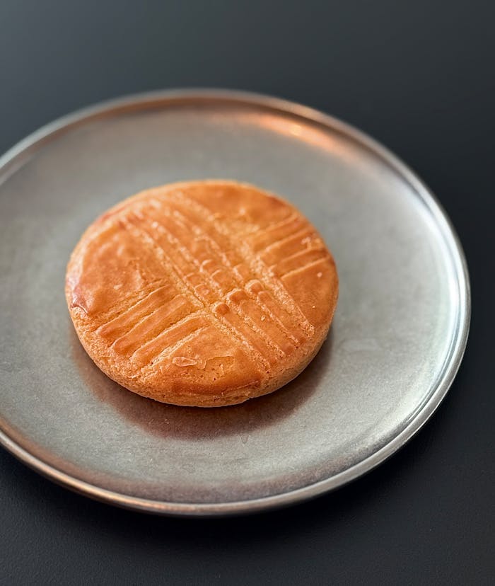 services-img Close-up of a traditional French sable cookie resting on a metal plate.