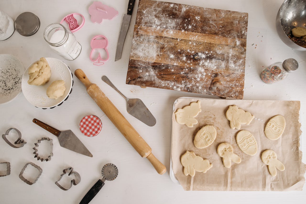 services-04 Top view of baking preparation with dough, cookie cutters, and utensils on a floured surface.